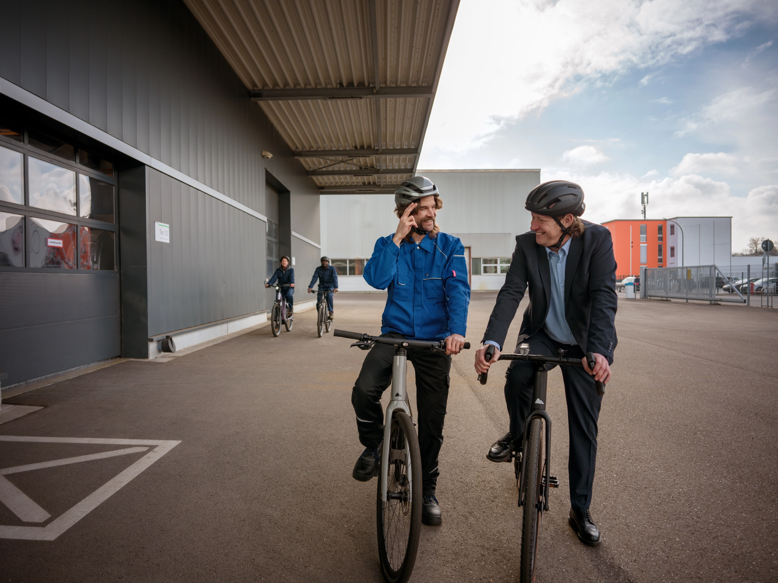 Mitarbeitende steigen zum Feierabend aufs Fahrrad auf einem Industriegelände Mitarbeitende steigen zum Feierabend aufs Fahrrad auf einem Industriegelände