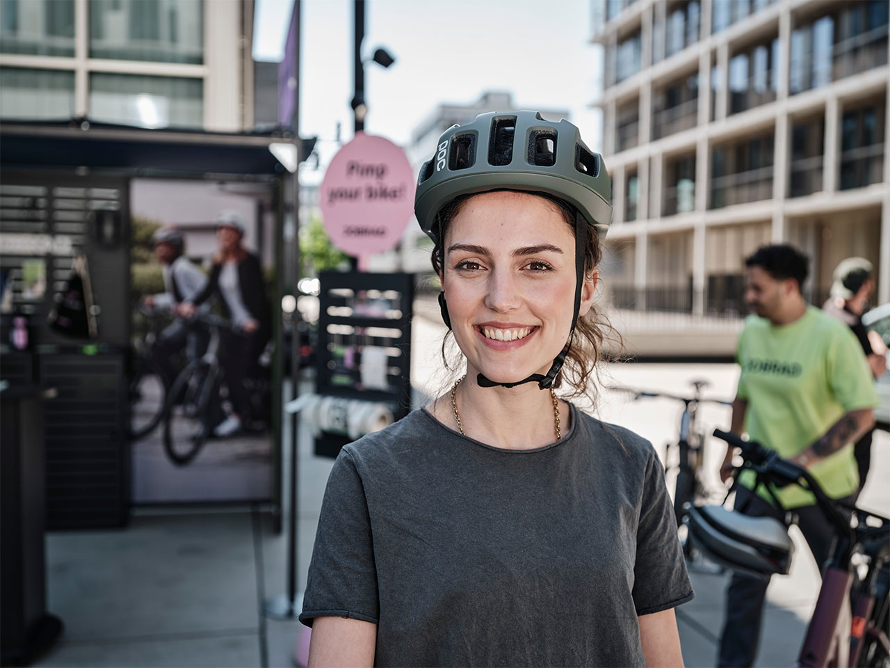Frau mit Helm auf dem Kopf schaut lächelnd in die Kamera vor Probefahrrädern Frau mit Helm auf dem Kopf schaut lächelnd in die Kamera vor Probefahrrädern